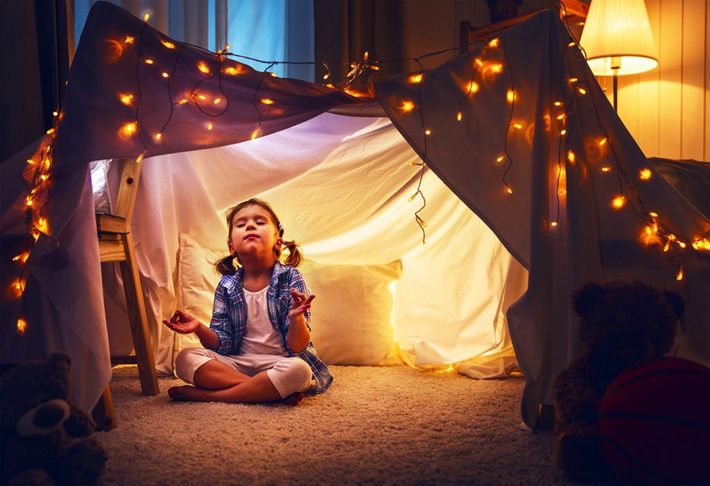 child girl playing meditates in yoga pose in tent at home