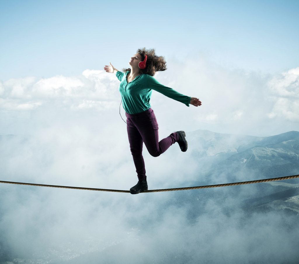 Woman balancing on a rope above clouds and mountains , while lis